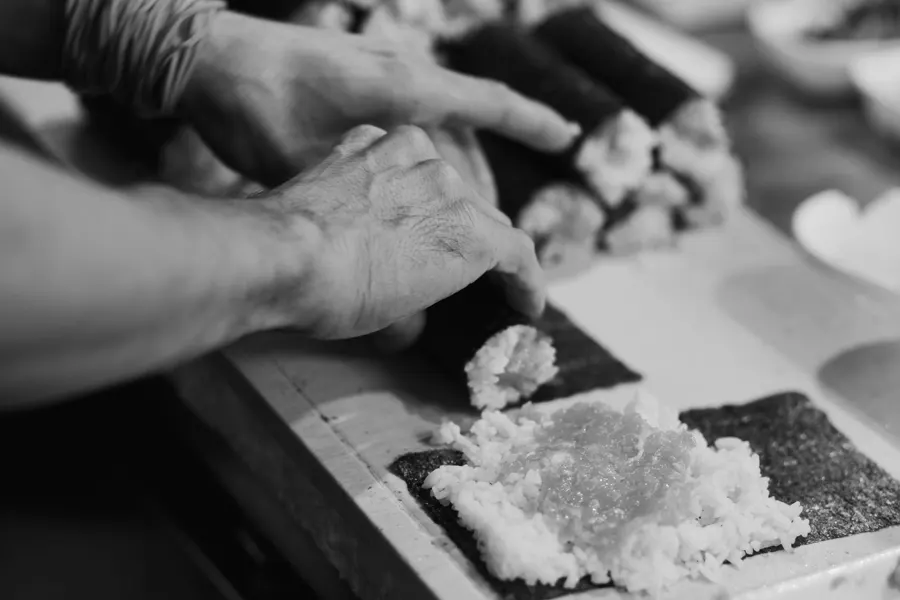 Mãos a espalhar arroz sobre a alga.