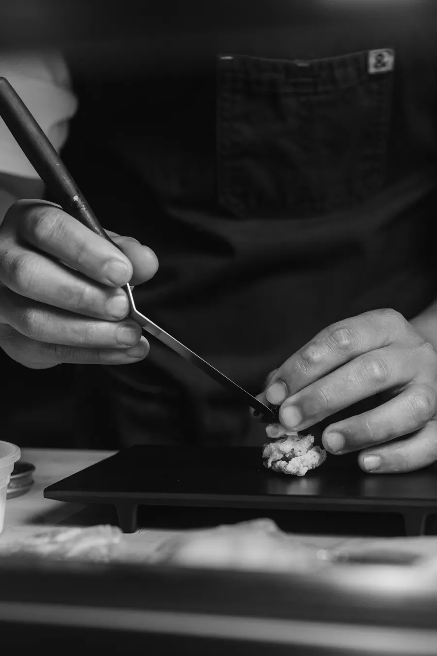 Mãos a pousar um pormenor num nigiri com uma pinça.