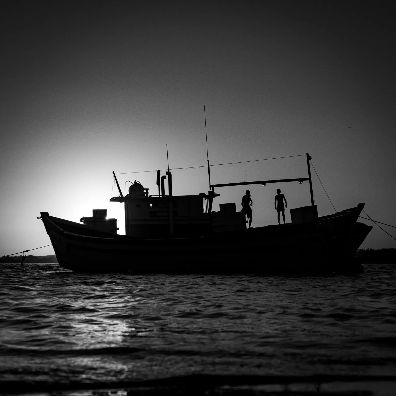 Barco de pesca no mar, a preto e branco, ao fim da tarde.