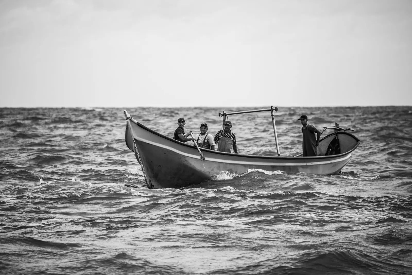Quatro pescadores num barco pequeno, em mar aberto, a preto e branco.